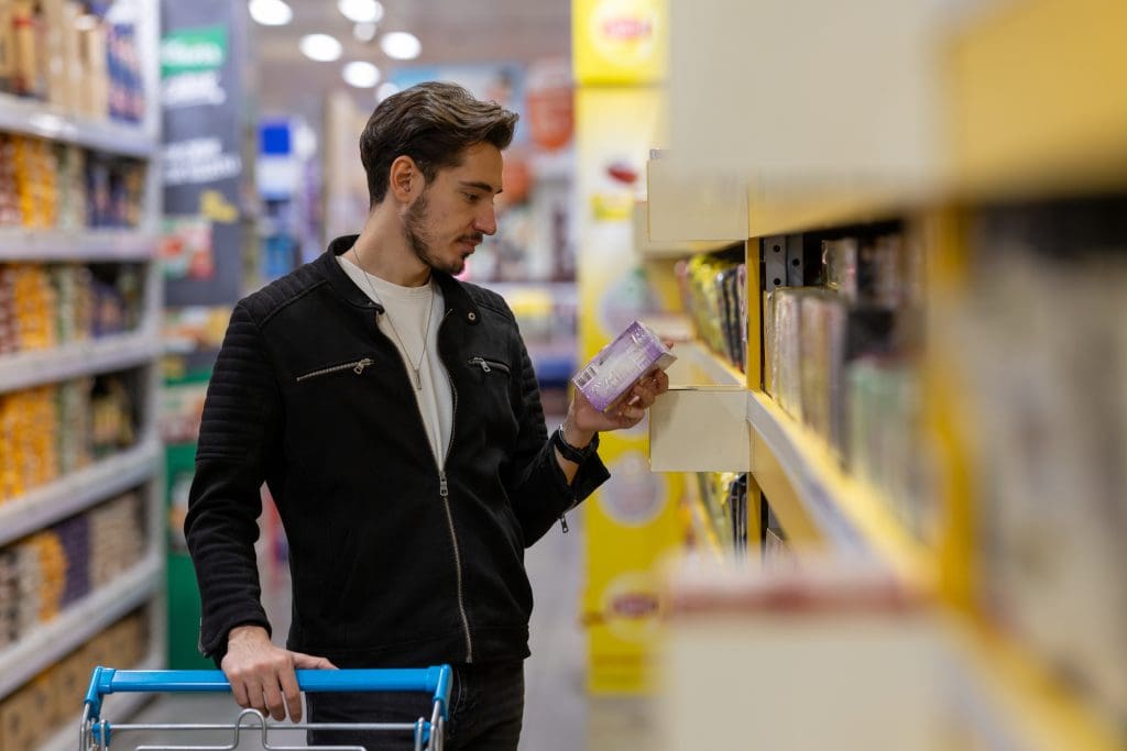 The young man examines the content of packaged foods in the supermarket - Mspark